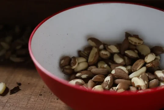 Tigela vermelha com castanhas-do-pará descascadas sobre uma superfície de madeira